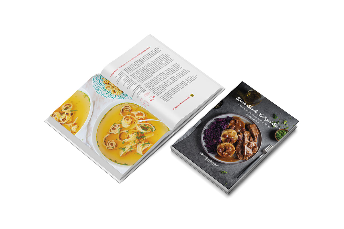 Auf einer weißen Fläche sind zwei Kochbücher „ESGE-Zauberstab Deutschlands-Leibgerichte“ abgebildet – eines geschlossen mit einem Gericht aus Fleisch, Kartoffeln und Rotkohl, das andere aufgeschlagen mit einem Suppenrezept mit Nudeln und Kräutern.