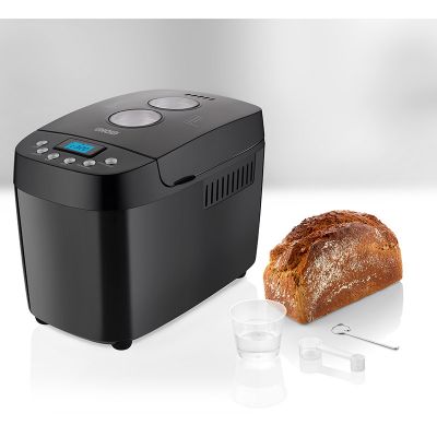 Ein schwarzer Brotbackautomat mit Digitalanzeige steht auf der Arbeitsplatte neben einem Laib Brot, einem Messbecher, einem Messlöffel und einem Knethaken.