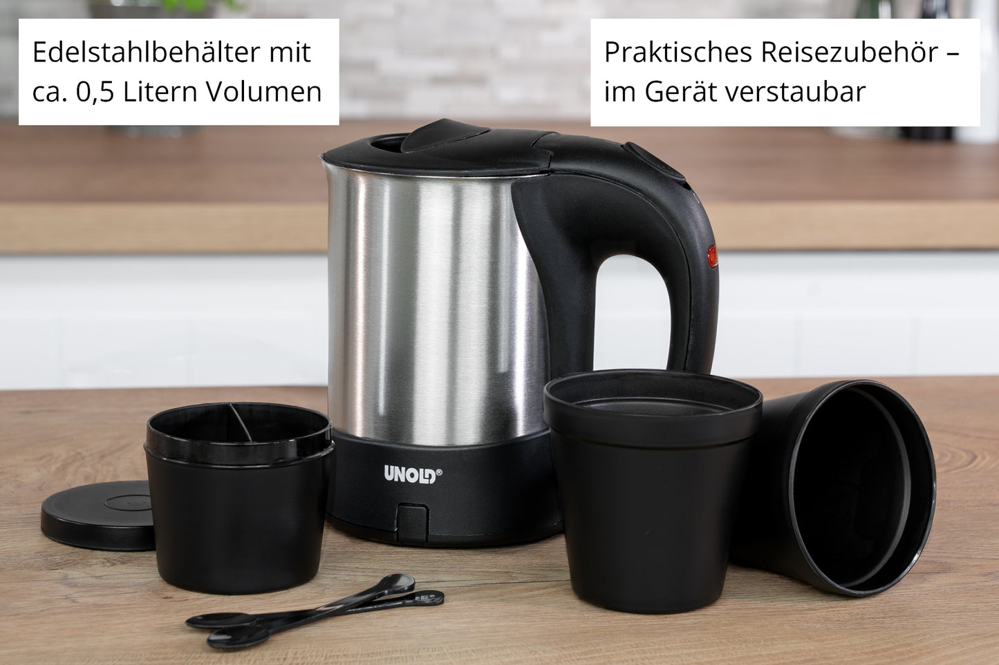 Der Unold Reiseblitzkocher Edelstahl 0,5 l steht auf einer Küchenarbeitsplatte mit einem schwarzen Griff, flankiert von zwei schwarzen Tassen, zwei Löffeln, einem kleinen Behälter und einem Deckel. Ein deutscher Text hebt das Fassungsvermögen von 0,5 l und das praktische Zubehör hervor.