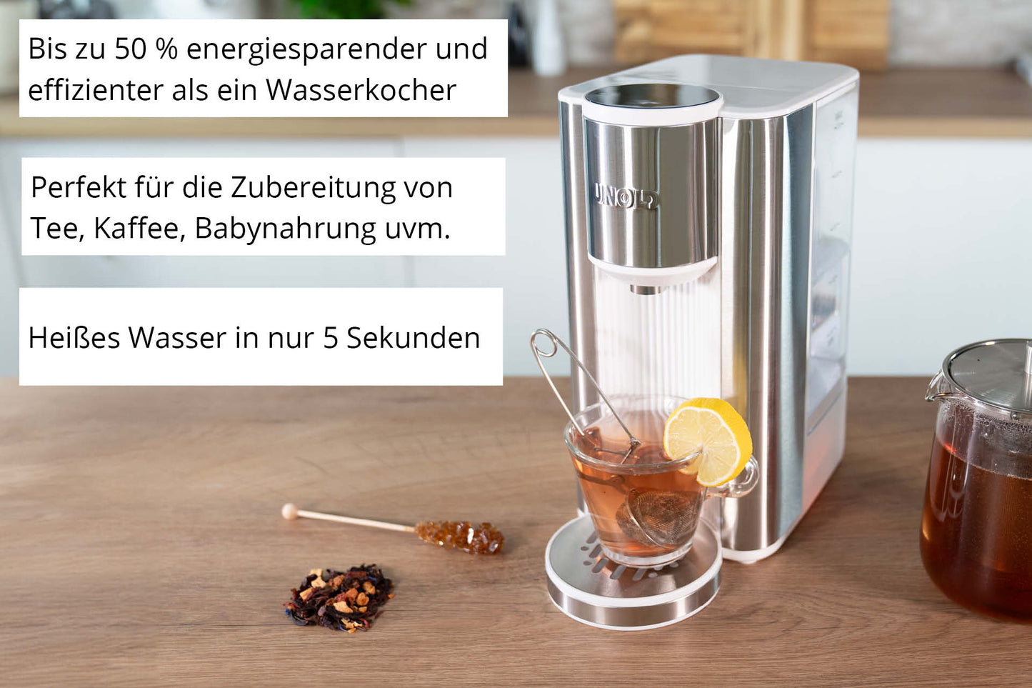 Der Unold Express Heißwasserbereiter Ava steht auf einer Holzplatte neben einer Teetasse mit Zitrone und einem Glas Honig. Das Gerät erhitzt Wasser schnell und energiesparend.