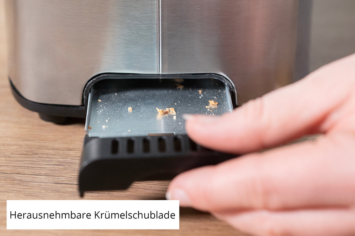 Eine Hand entnimmt die kleine Krümelschublade aus Metall mit Brotkrümeln aus dem Unold Toaster Thommy. Die deutsche Aufschrift lautet „Herausnehmbare Krümelschublade“.