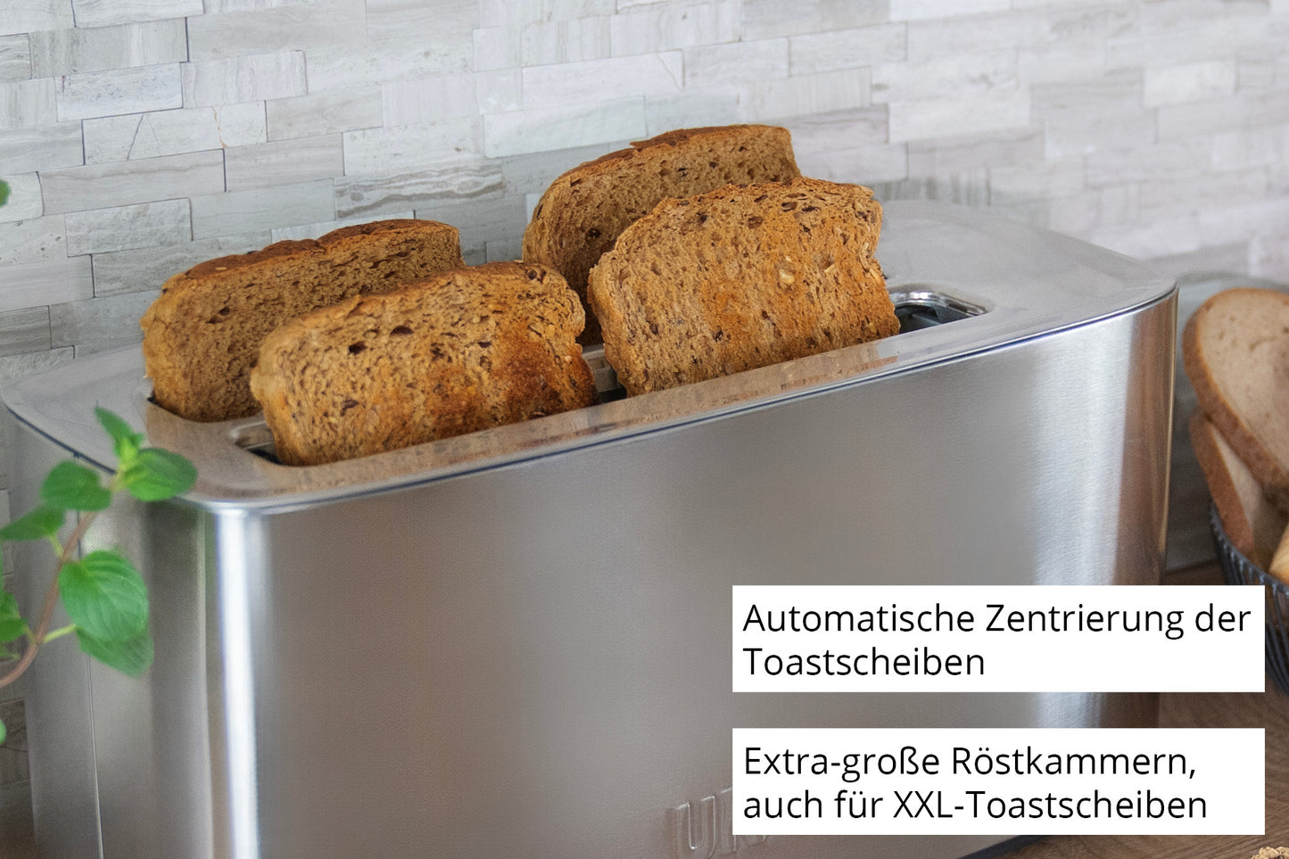 Der Unold Toaster Tom in Silber toastet vier große Scheiben Vollkornbrot. Der deutsche Text hebt die automatische Zentrierung und die extragroßen Schlitze für XXL-Toast hervor. Hintergrund: hell geflieste Wand mit einer grünen Pflanze.
