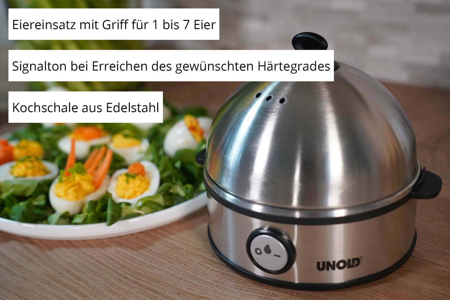 Der Unold Eierkocher Edel aus Edelstahl steht auf der Küchentheke, daneben ein Teller mit dekorierten gekochten Eiern und Gemüse. Der deutsche Text hebt die wichtigsten Funktionen dieses Unold-Geräts hervor.