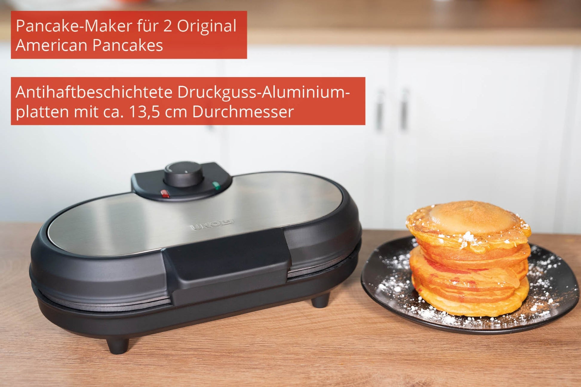 Der Unold Pancake-Maker American steht auf einer Holztheke neben einem Teller mit goldenen Pfannkuchen, und ein rotes deutsches Etikett hebt seine Funktionen und Größe hervor.