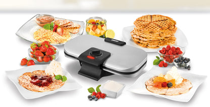Der Unold Doppel-Waffelautomat steht auf einer weißen Fläche, umgeben von Tellern mit Waffeln, frischen Erdbeeren, Beeren, Schlagsahne, Puderzucker, Sirup und Früchten in Glasschalen.