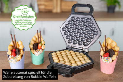 Der Unold Bubble Waffeleisen Bobby steht offen auf der Küchentheke und lädt mit goldenen Bubble Waffeln zum Verweilen ein. Drei Waffeln in bunten Bechern sind mit Früchten, Keksen und Stäbchen gefüllt, während ein deutscher Text die Funktionen des Geräts hervorhebt.