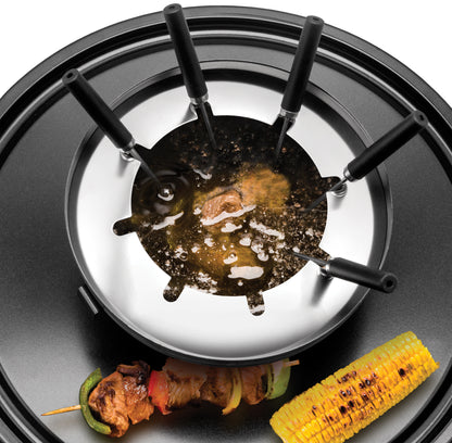Das Unold Raclette Multi 4 in 1 inklusive Raclette Buch steht auf einem schwarzen Tablett mit sechs Gabeln mit schwarzen Griffen, heißem Öl darin, dazu ein gegrillter Maiskolben und ein Spieß mit Fleisch und Gemüse.