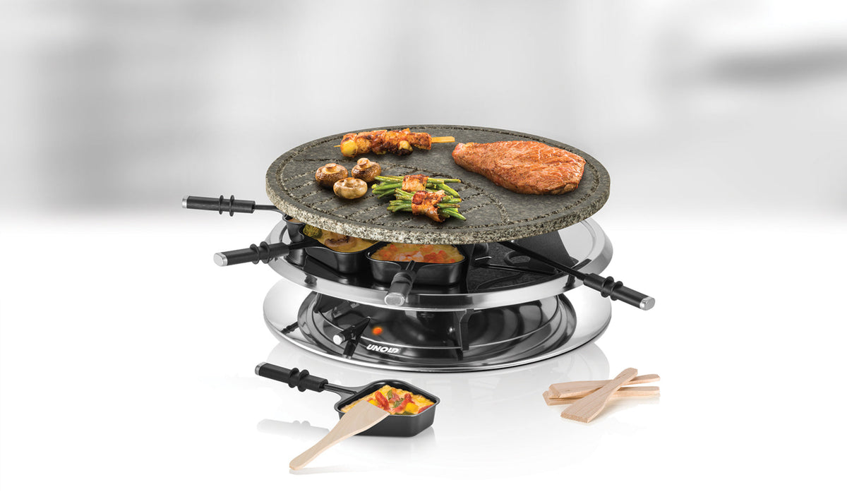 Das Unold Raclette Multi 4 in 1 inklusive Raclette Buch verfügt über eine Steinplatte zum Grillen von Fleisch, Gemüse und Spießen. Um den Edelstahlsockel herum sind Pfännchen und Holzspatel angeordnet.