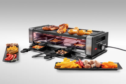Das Unold Raclette Finesse Basic inklusive Raclette Buch besteht aus gekochtem Hähnchen, Kartoffeln und Gemüse auf der Oberseite, auf vier Tabletts befinden sich Käse und Gemüse. Davor stehen zwei schwarze Teller mit verschiedenen Gemüsescheiben.