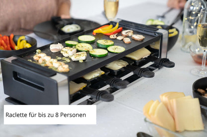 Mit dem Unold Raclette Finesse Basic können bis zu 8 Personen Gemüse und Käse oben grillen, während kleine Tabletts darunter stehen. Teller mit Käsescheiben und Gemüse runden den Tisch ab. Bildunterschrift: Raclette für bis zu 8 Personen.