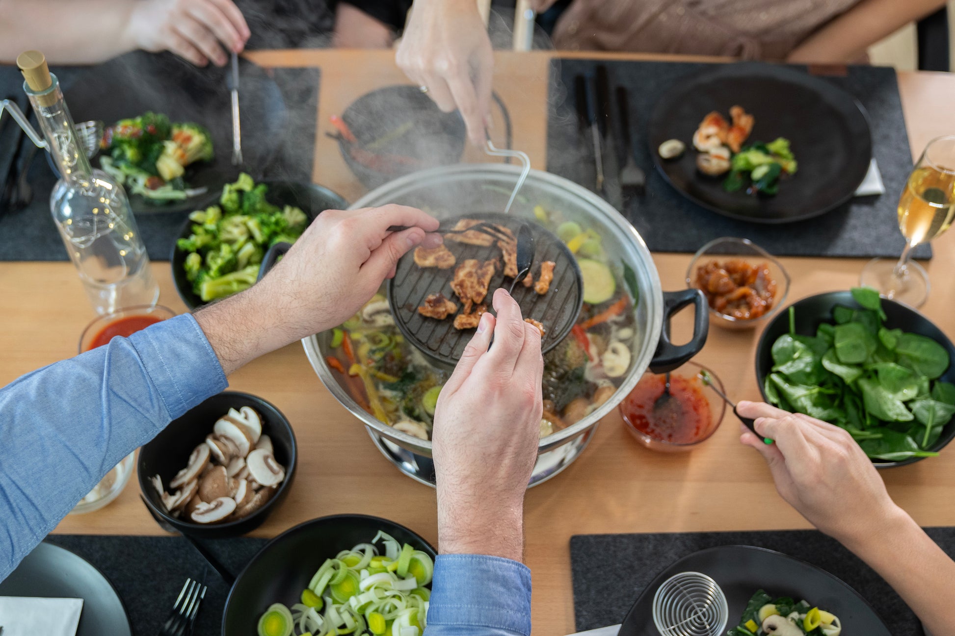 Vier Personen genießen ein Asia-Fondue mit dem Unold Hot Pot, bei dem Fleisch und Gemüse in die brodelnde Brühe gegeben werden. Teller mit frischem Gemüse, Pilzen, Saucen und Getränken runden das Herzstück ab und sorgen für ein lebendiges gemeinsames Essenserlebnis.