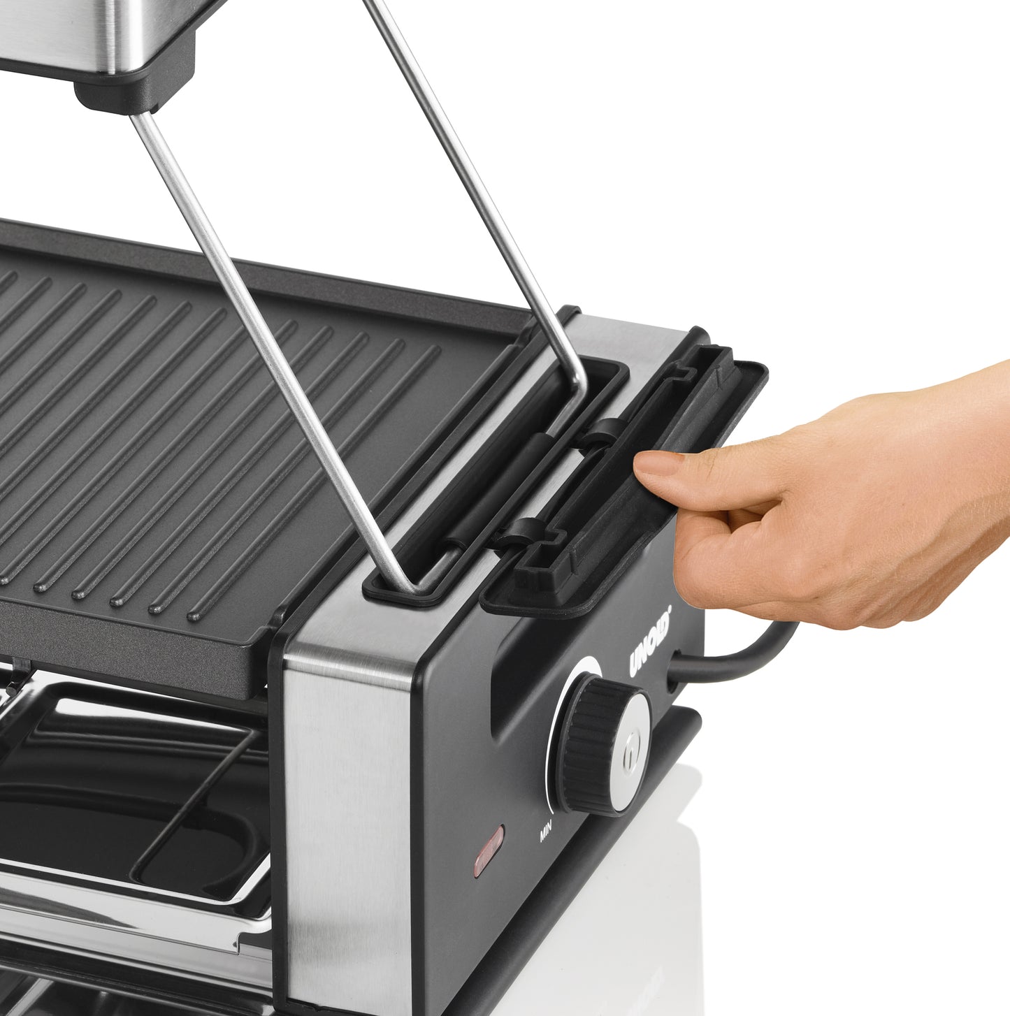 Beim Öffnen des Deckels des Unold Raclette Smokeless inklusive Raclette Buch kommt die geriffelte Grillfläche zum Vorschein. Das silber-schwarze Gerät verfügt über einen Bedienknopf und eine Kontrollleuchte an der Vorderseite.