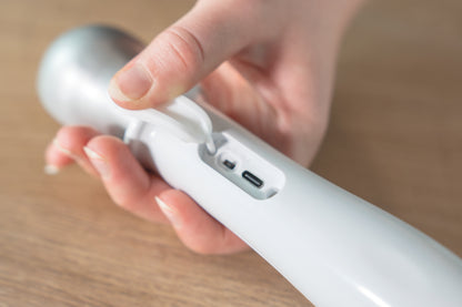 Eine Hand hebt die Gummiabdeckung des Unold Beheizten Eisportionierers Carlo an und gibt den Blick auf den Ladeanschluss mit USB-C und einen weiteren kleinen Anschluss frei, der vor einem Holzhintergrund angebracht ist.