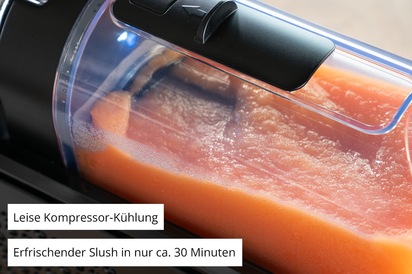 Nahaufnahme der Unold Slush-Eismaschine Stella, gefüllt mit orangefarbenem Slush. Deutscher Text auf dem Bild: "Leise Kompressor-Kühlung" und "Erfrischender Slush in nur ca. 30 Minuten.