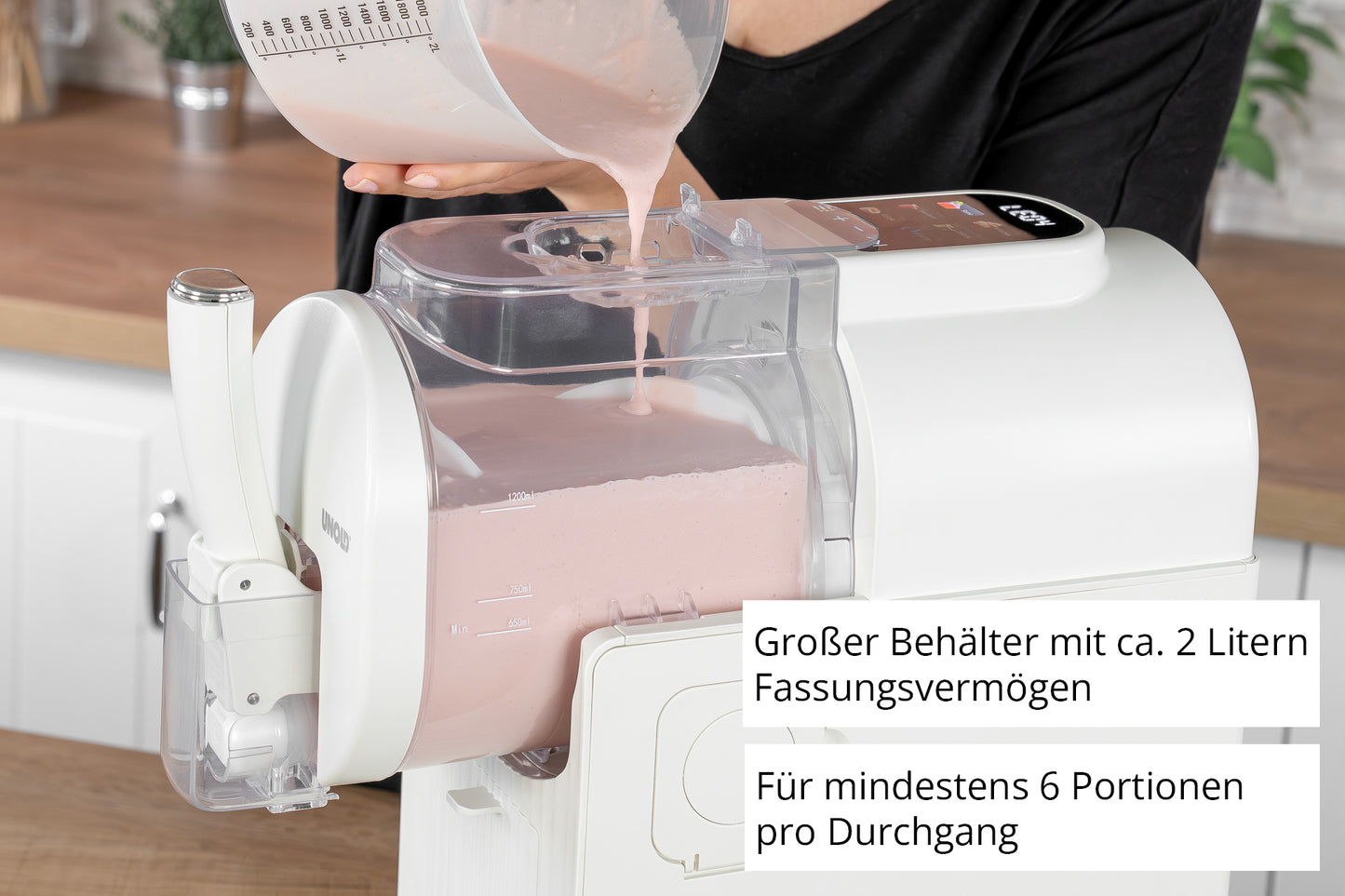 Eine Person gießt einen rosa Smoothie in die Unold Slusheismaschine Sofia, die über einen großen transparenten 2-Liter-Behälter verfügt und mindestens 6 Portionen pro Gebrauch zubereiten kann, wie durch den deutschen Text hervorgehoben wird.