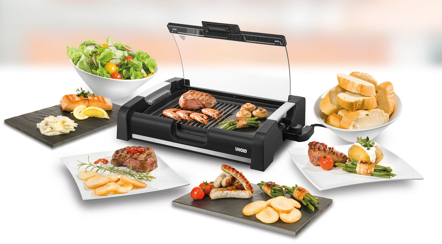 Ein elektrischer Tischgrill mit verschiedenen gegrillten Fleischsorten und Gemüse, umgeben von Tellern mit Salat, Brot, Fisch, Steak und Beilagen, präsentiert auf einer weißen Oberfläche.