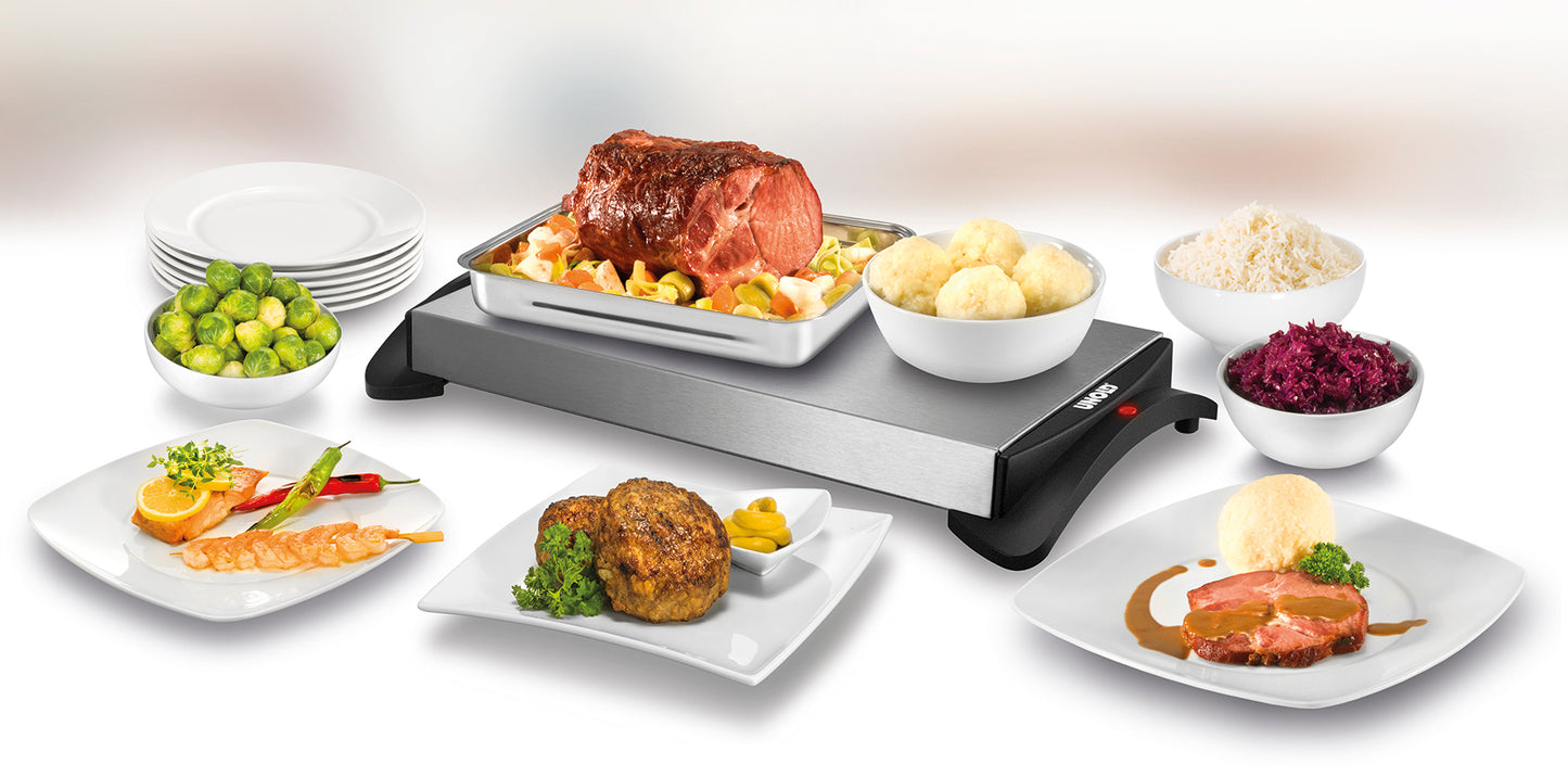 Als Buffet wird die Unold-Warmhalteplatte serviert, ein vorgewärmtes Tablett mit Braten und Gemüse, umgeben von Tellern mit Rosenkohl, Knödeln, Reis, Rotkohl, Lachs, gemischtem Gemüse, einem Frikadellenstück und Bratenaufschnitt.