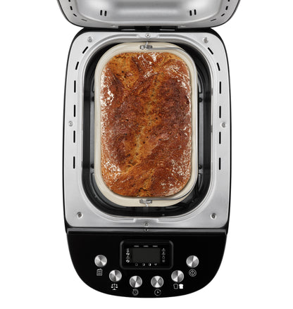 Ein frisch gebackenes, goldbraunes Brot mit einer mit Mehl bestäubten Kruste und dunklen Krustenwirbeln liegt im Inneren des Unold Backmeister® Big Brotbackautomaten, von oben betrachtet bei geöffnetem Deckel.