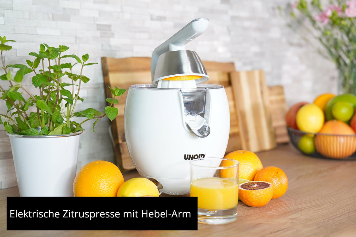 Die Unold ZITRUSPRESSE Power Juicy, eine weiße elektrische Zitruspresse mit Hebelarm, steht auf einem Küchentisch inmitten von frischen Orangen, Orangensaft, Minze und Zitrusfrüchten. Deutscher Text: Elektrische Zitruspresse mit Hebel-Arm.