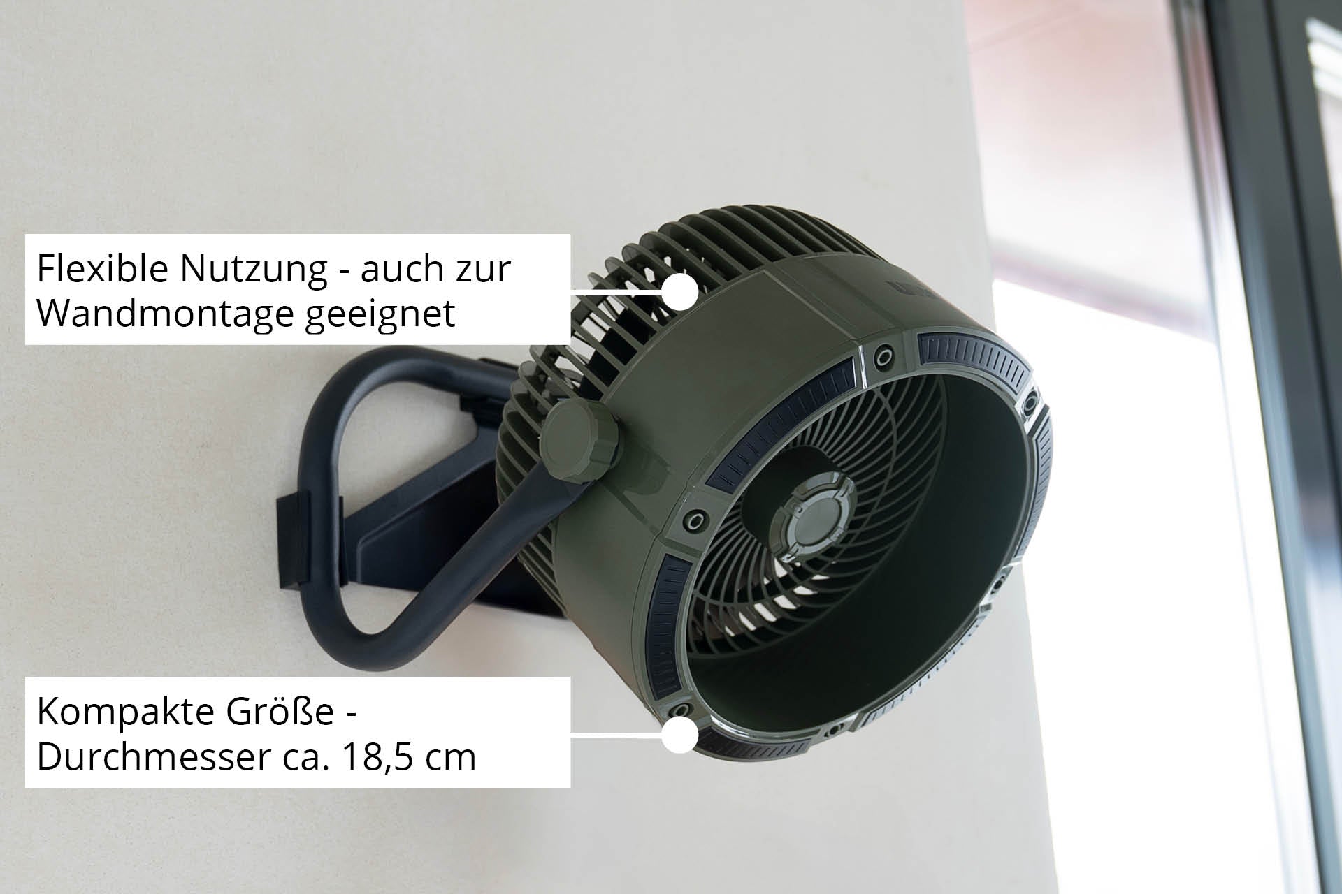 Der Unold Akkuventilator Outdoor ist ein kompakter, dunkelgrün-schwarzer Ventilator mit ca. 18,5 cm Durchmesser, konzipiert für den flexiblen Einsatz und die einfache Wandmontage, wie im deutschen Text dargestellt, in Fensternähe.