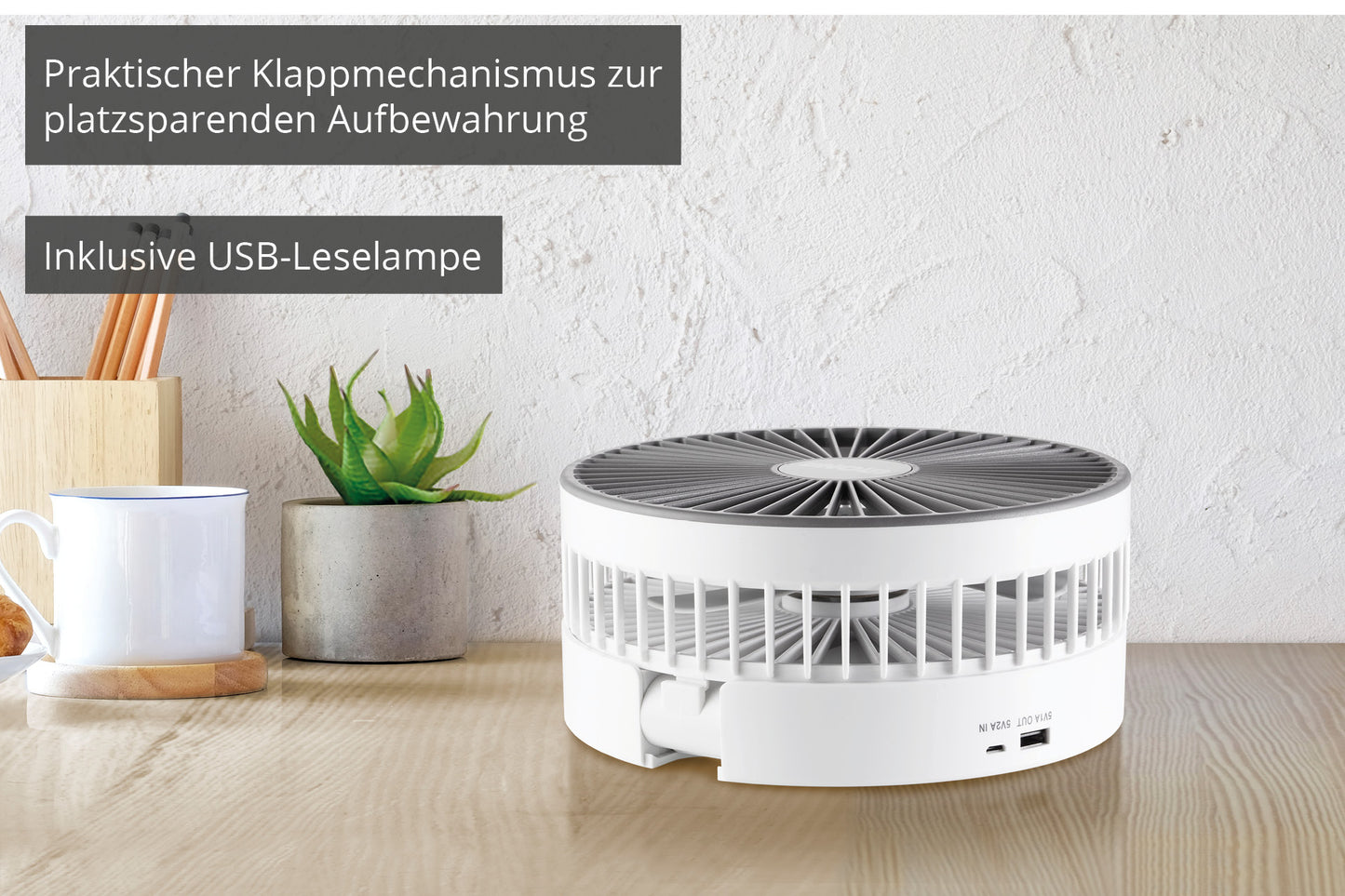 Der Unold TELESKOP-VENTI CORDLESS, ein weißer, runder Ventilator mit USB-Anschluss, steht auf einem Holztisch neben einer Tasse, einer Pflanze und Utensilien. Deutscher Text hebt das faltbare Design und die mitgelieferte USB-Leselampe hervor.