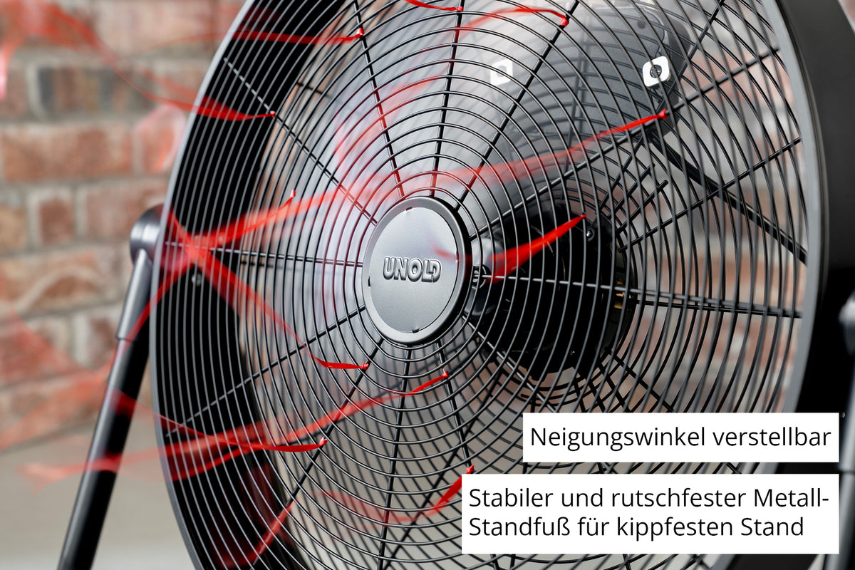 Nahaufnahme des Unold Windmaschine Black Steel Standventilators mit roten Luftstromlinien, verstellbarer Neigung und einem stabilen, rutschfesten Metallsockel. Vor dem Hintergrund einer Backsteinmauer.
