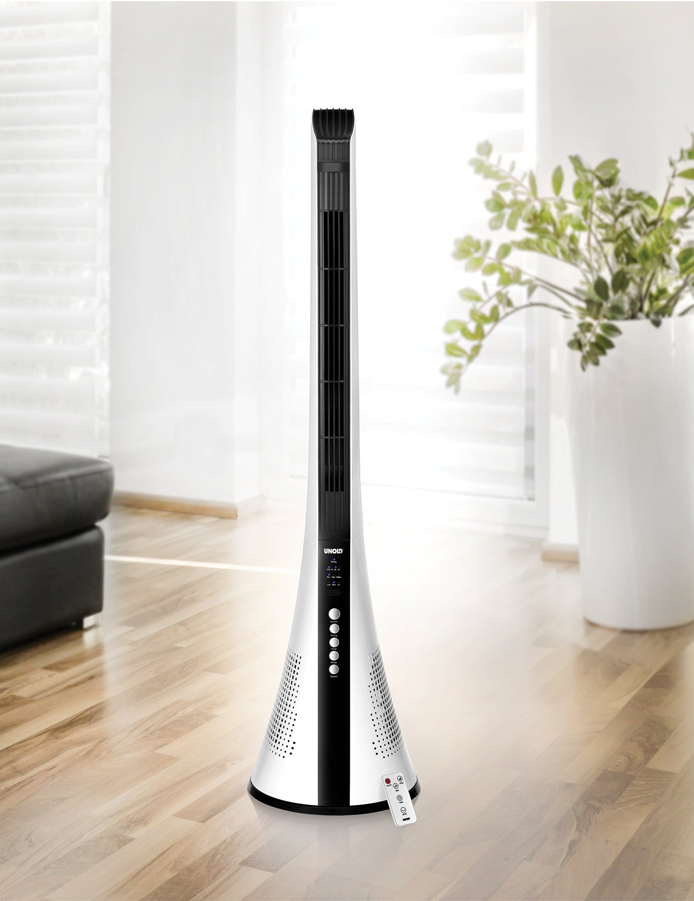 Der Unold TURMVENTILATOR VIEW, ein moderner schwarz-weißer Turmventilator mit Bedienknöpfen und Fernbedienung, steht auf einem Holzboden in einem hellen Wohnzimmer mit Sofa, großen Fenstern und einer Topfpflanze im Hintergrund.