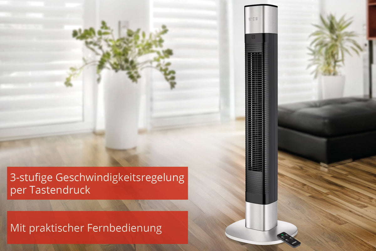 Der Unold TURMVENTILATOR EDEL in Schwarz und Silber steht auf Holzboden in einem hellen Wohnzimmer. Deutscher Text hebt 3 Geschwindigkeitsstufen und eine praktische Fernbedienung hervor, die neben dem Ventilator auf dem Boden liegt.