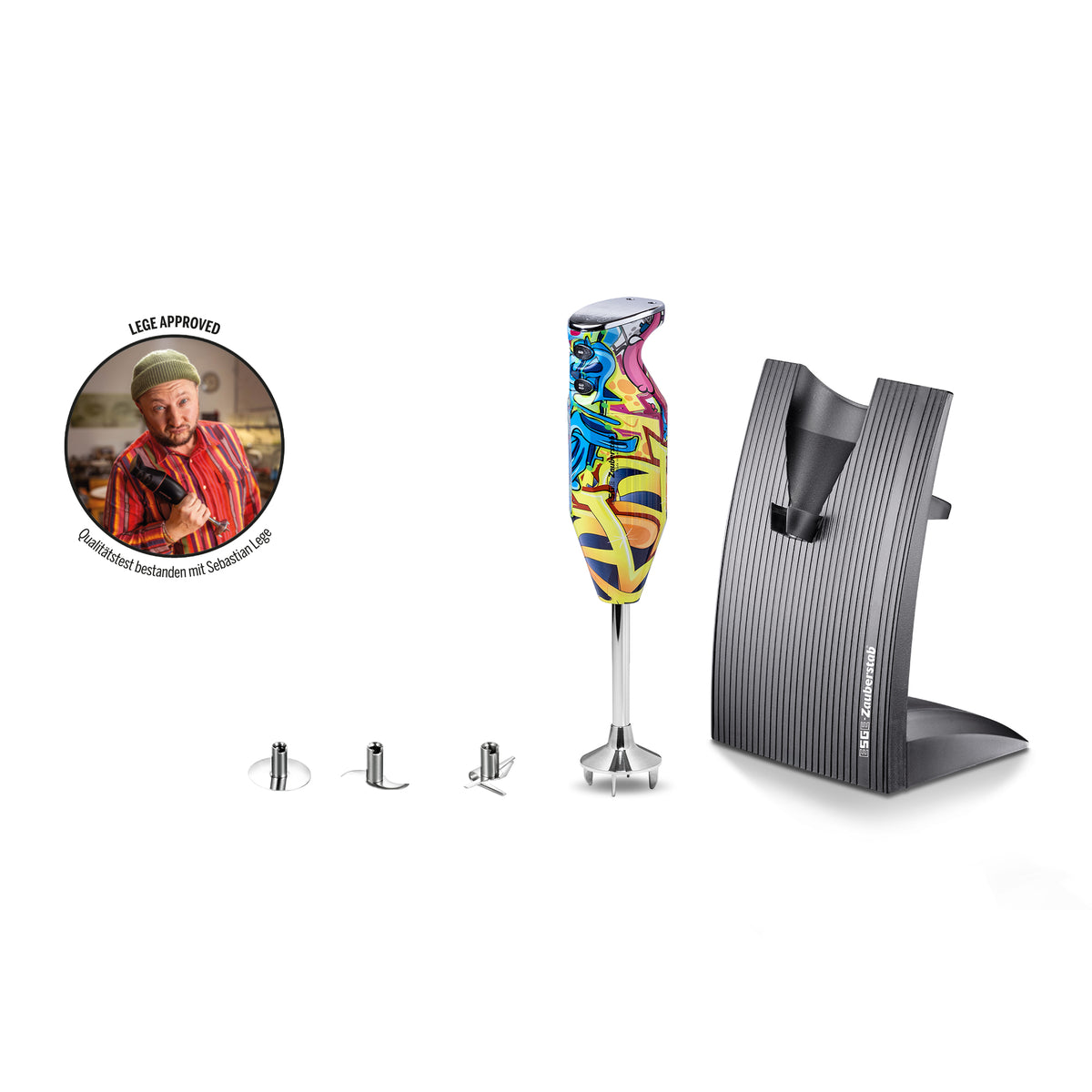 Der Stabmixer „ESGE-Zauberstab Design Edition Pop Art“ von ESGE-Zauberstab besticht durch ein farbenfrohes, von Graffiti inspiriertes Design und wird mit einem Ständer, drei Metallaufsätzen sowie einem runden „Löwe Approved“-Abzeichen geliefert, auf dem ein Koch in rotem Hemd und Kochmütze abgebildet ist. Alle Artikel sind vor einem weißen Hintergrund angeordnet.