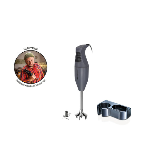 Ein anthrazitfarbener Stabmixer „ESGE-Zauberstab M 100 – Exklusiv Edition“ von ESGE-Zauberstab, inklusive Wandhalterung, Messeraufsatz und einem kleinen runden Anstecker mit der Abbildung eines Kochs, der den Daumen hochhält, sowie einem Text in einer anderen Sprache.