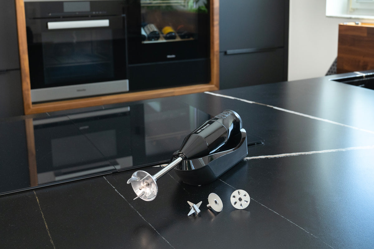 Der kabellose Stabmixer Schwarz 95105 von Unold ESGE-Zauberstab® mit Aufsätzen steht auf einer eleganten schwarzen Arbeitsplatte, im Hintergrund sind moderne Küchengeräte zu sehen.