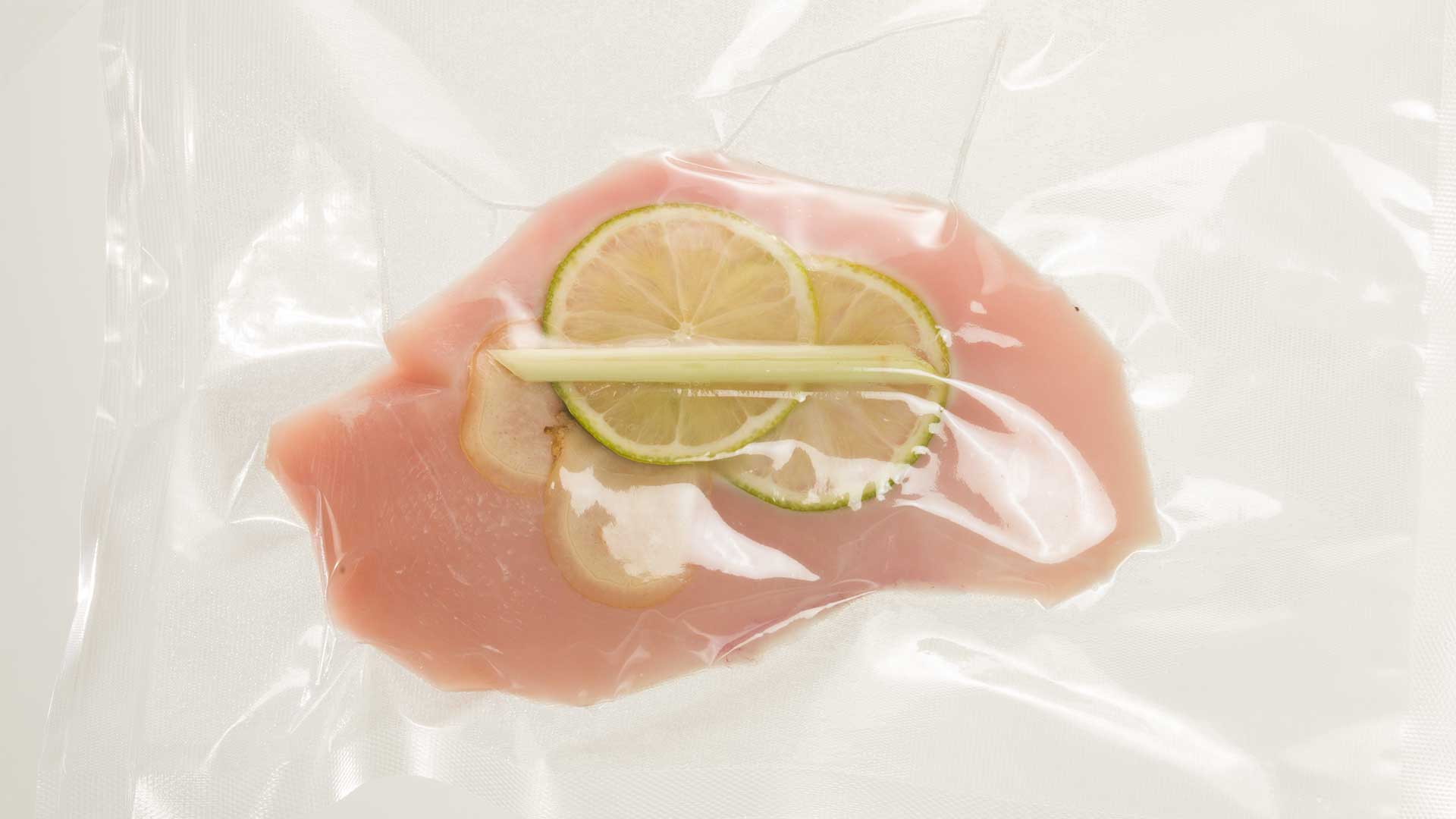 Rohe Hähnchenbrust in einem vakuumversiegelten Beutel mit Limettenscheiben und einer Stange Zitronengras darauf, bereit zum Sous-Vide-Garen.