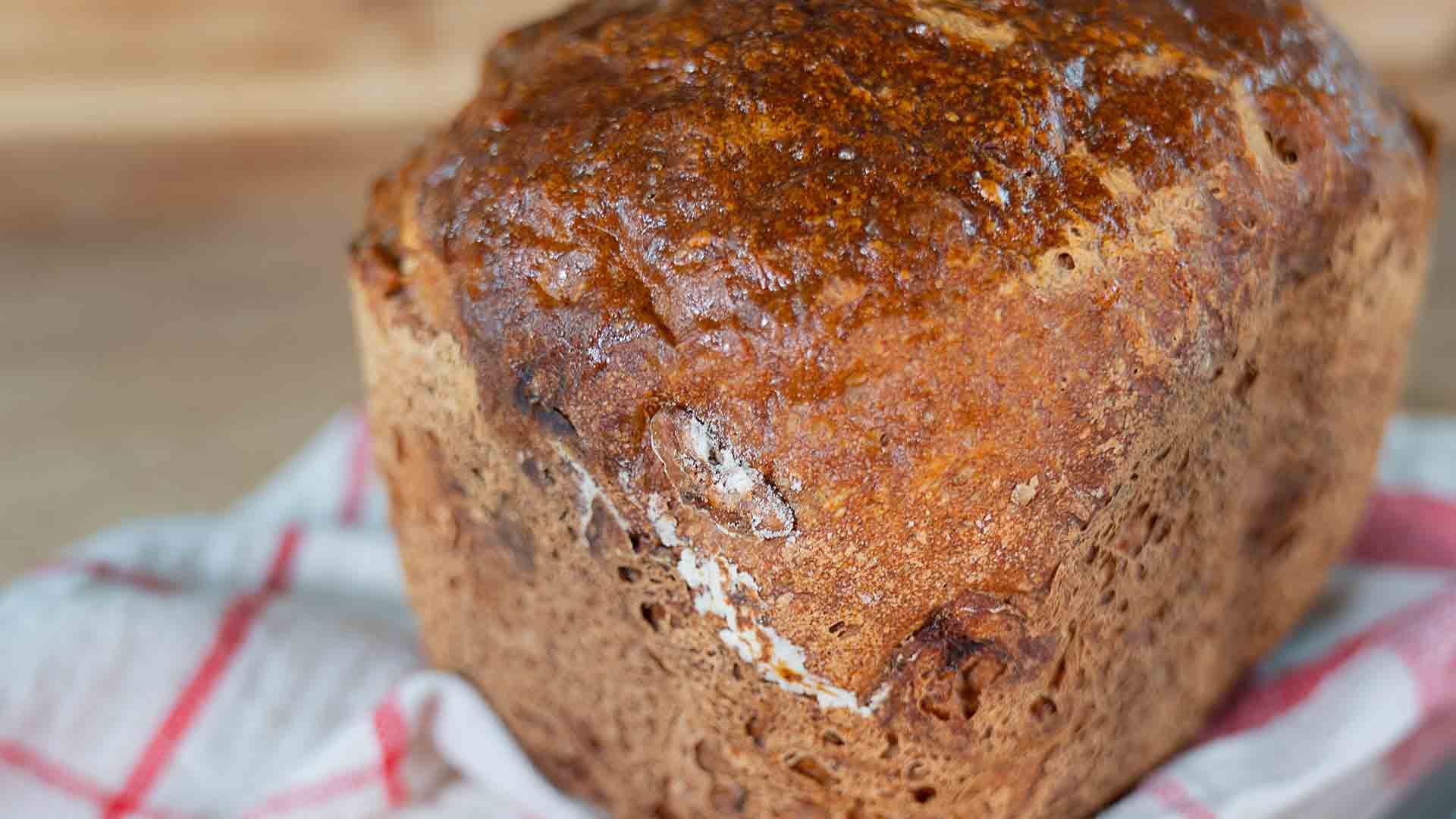 Eine Nahaufnahme eines frisch gebackenen Brotlaibs mit goldbrauner Kruste, der auf einem weiß-rot karierten Tuch liegt.
