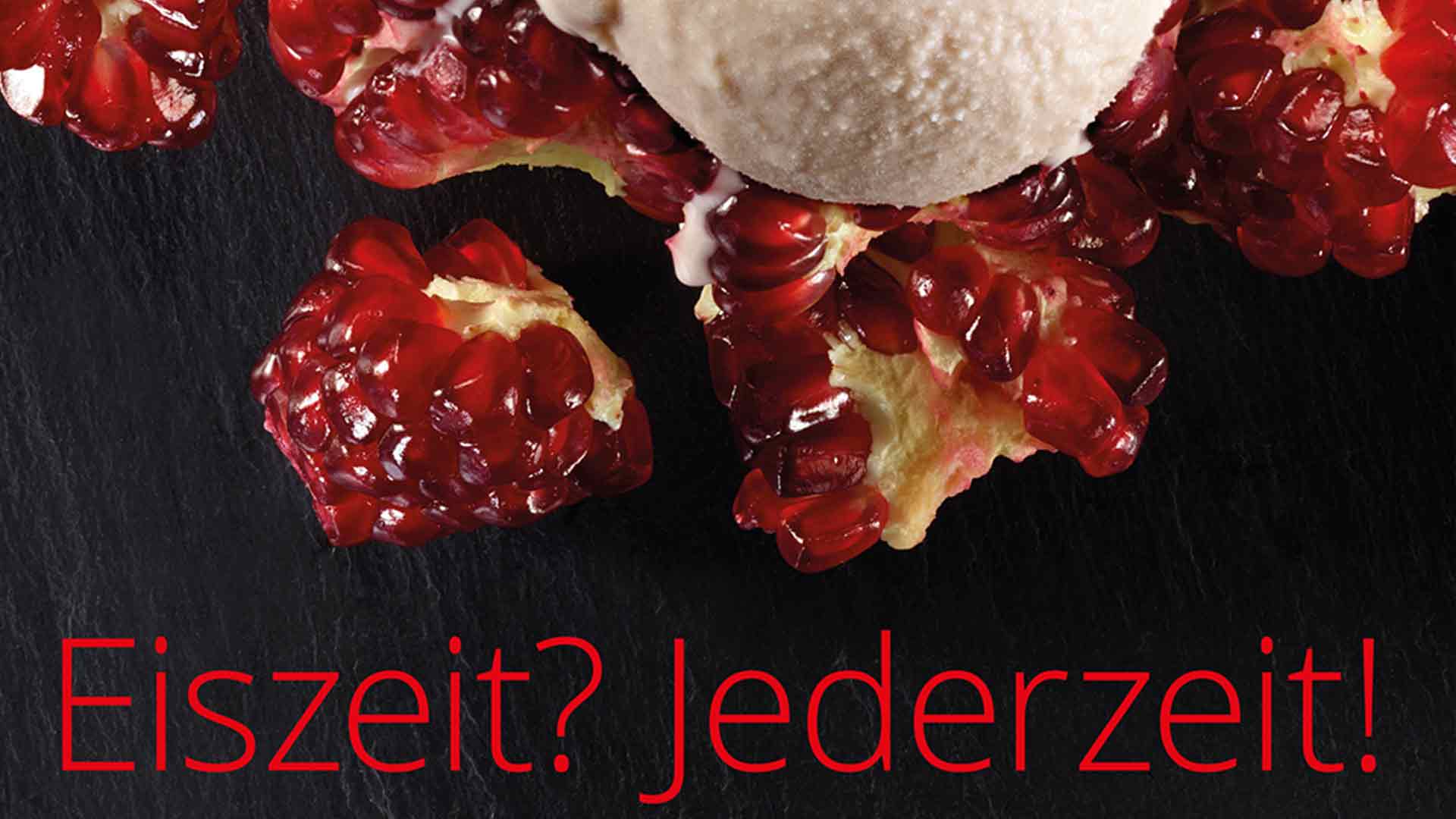 Eine Kugel Eis liegt auf Granatapfelkernen auf einer dunklen Oberfläche. Unten steht in kräftigem Rot: „Eiszeit? Jederzeit!“.
