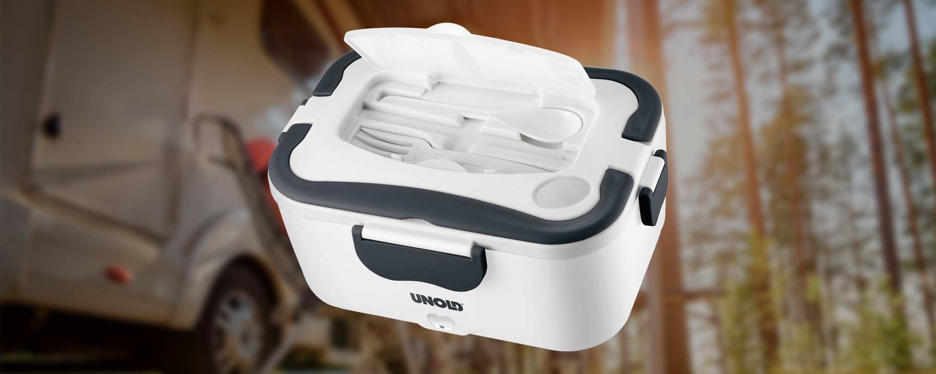 Eine tragbare elektrische Lunchbox in Weiß und Schwarz mit einem Fach für Besteck, geöffnet gezeigt mit einer Gabel und einem Löffel darin, vor einem unscharfen Außenhintergrund mit Bäumen und einem Wohnmobil.