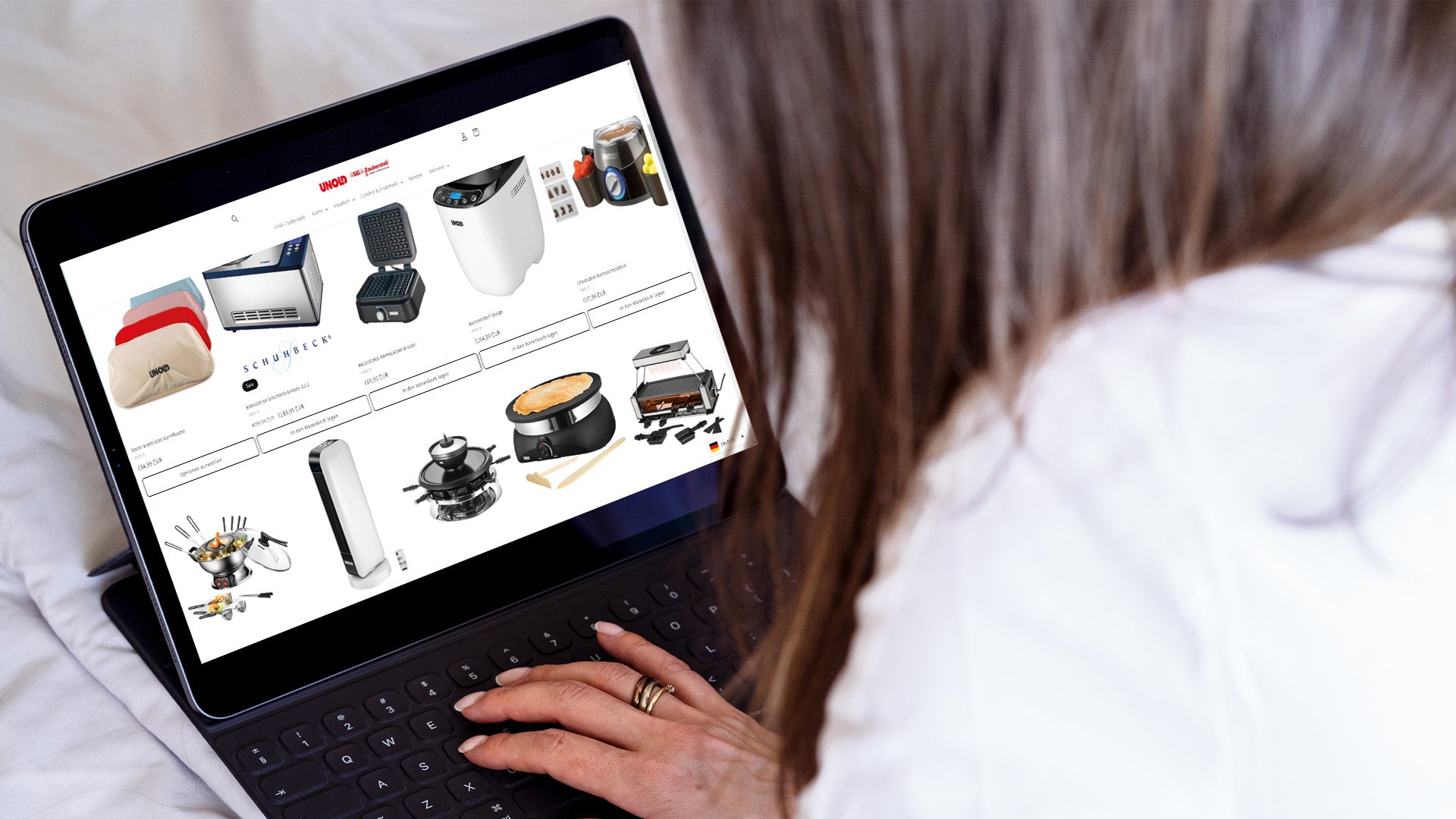 Eine Person durchsucht mithilfe eines Tablets die Seite eines Online-Shops, auf der verschiedene Haushalts- und Küchengeräte angezeigt werden, darunter ein Toaster, ein Wasserkocher, ein Reiskocher und eine Kaffeemaschine.