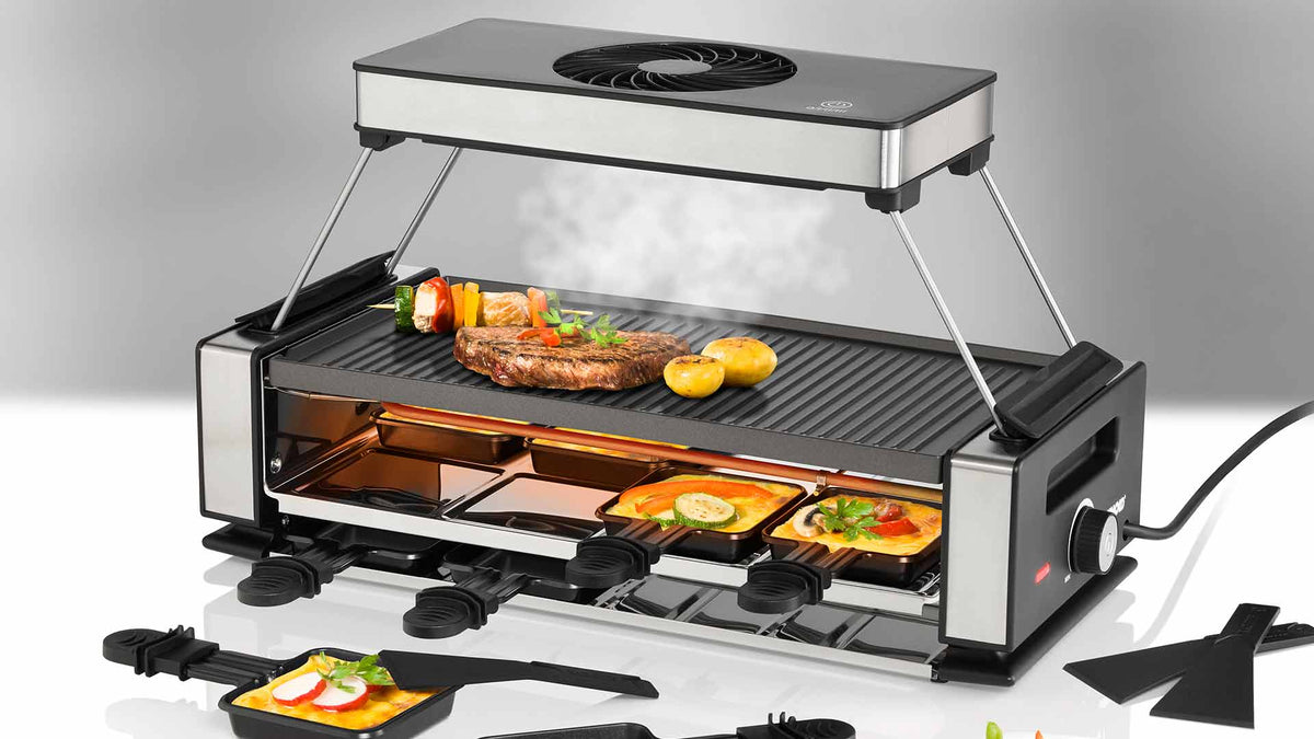 Ein elektrischer Tischgrill, auf dem Spieße, Steaks und Gemüse gegart werden, während darunter kleine Schalen mit geschmolzenem Käse und Beilagen erhitzt werden. Man sieht, wie Dampf vom Grill aufsteigt.