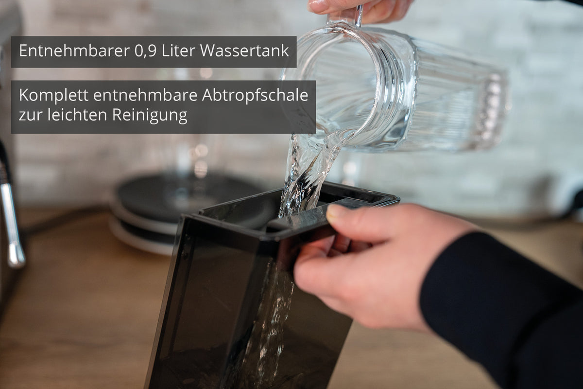 Eine Person gießt Wasser aus einer Glaskanne in den abnehmbaren 0,9-Liter-Wassertank der Unold Espressomaschine Piccopresso, während der Bildtext den leicht zu reinigenden abnehmbaren Tank und die Tropfschale hervorhebt.