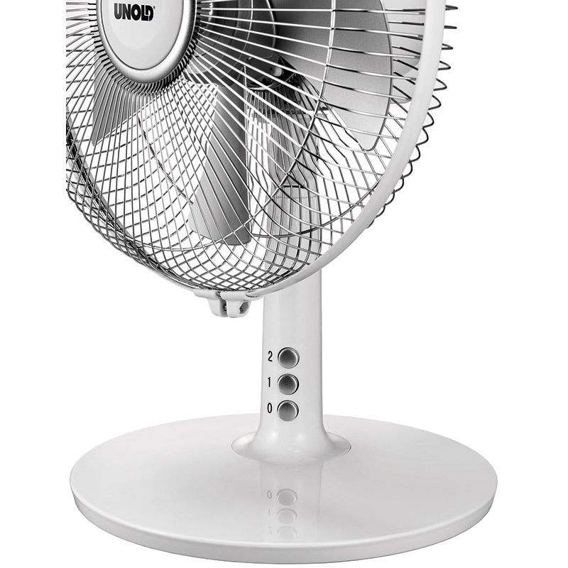 Eine Nahaufnahme eines Unold TISCHVENTILATOR SILVERLINE-Standventilators zeigt sein Gitter, die mit 0, 1 und 2 beschrifteten Steuertasten auf dem Ständer und das Unold-Logo in der Mitte.