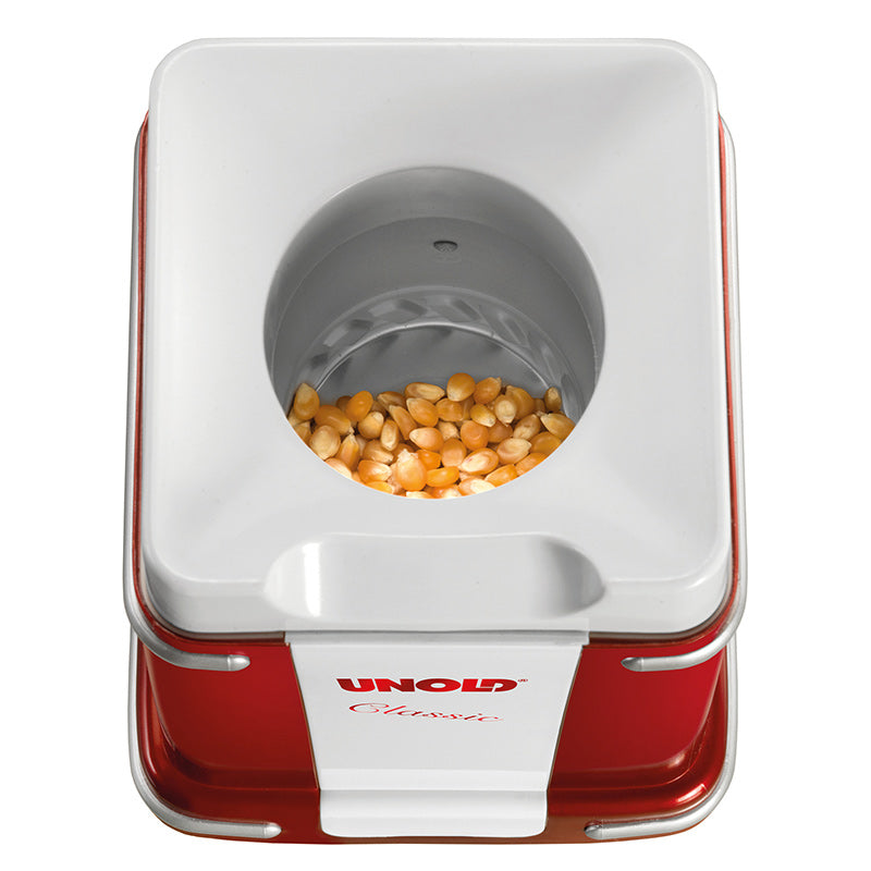 Draufsicht auf einen rot-weißen Unold Popcornmaker Classic, der in der runden Kammer mit ungepoppten Maiskörnern gefüllt ist.