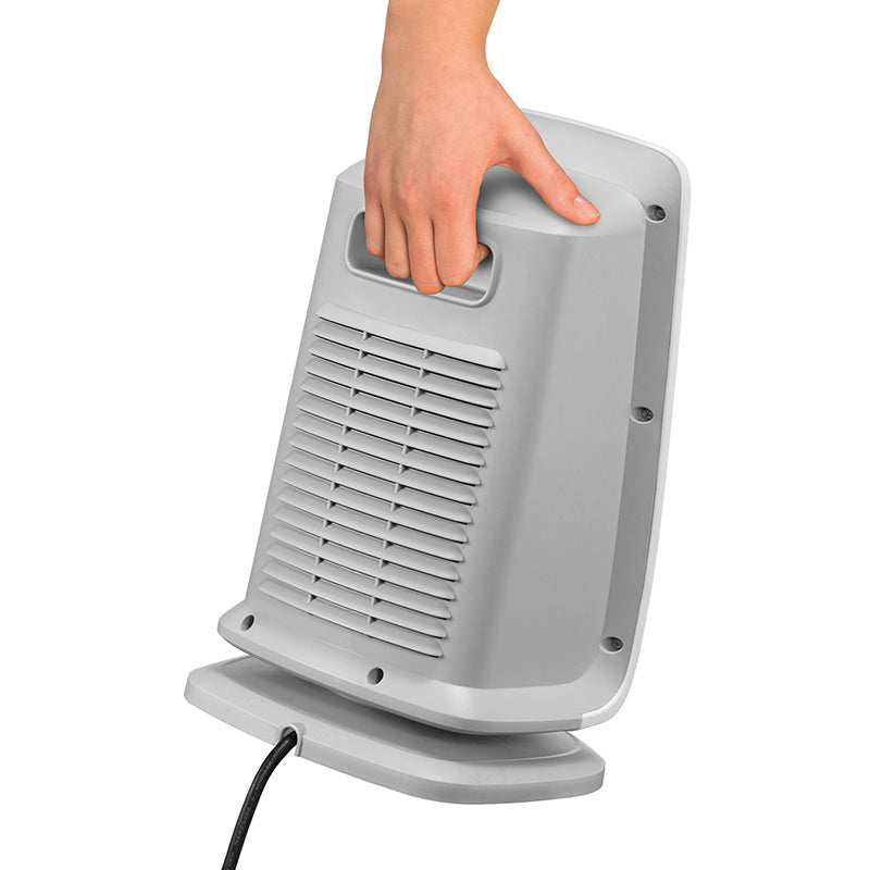 Eine Hand hält den Griff eines Unold KERAMIK-HEIZLÜFTER BAD, eines tragbaren grauen elektrischen Heizgeräts, von hinten betrachtet, mit sichtbarem Netzkabel.