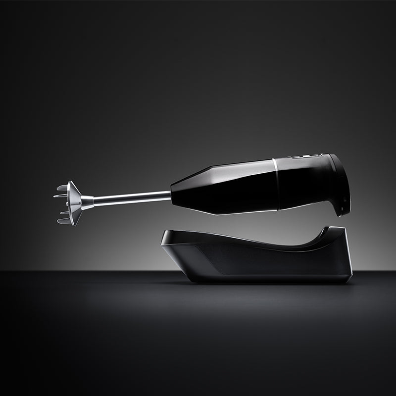 Der kabellose Stabmixer Unold ESGE-Zauberstab® PLUS Schwarz liegt horizontal auf einem passenden Ständer vor einem dunklen, abgestuften Hintergrund und präsentiert sein modernes und minimalistisches schwarzes Design.